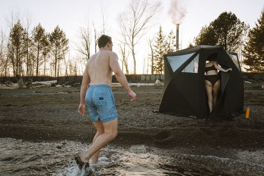 Portable North Shore sauna tent set up for contrast therapy with an adjacent cold plunge barrel on a wooded lakeshore.